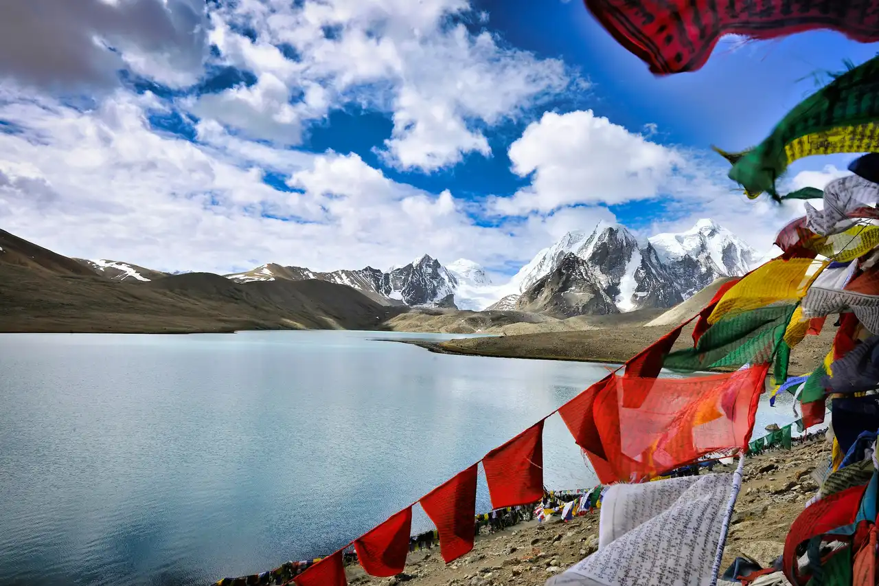 Prayer flags strung above a still high-altitude lake, snow peaks behind